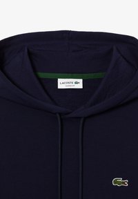 Felpa blu navy realizzata in cotone, con cappuccio interno a righe verdi e un piccolo logo di coccodrillo ricamato sul petto. Vestibilità classica.