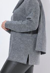 Grijze gebreide trui met een col, geribbelde textuur, zijinkepingen en een losse pasvorm, gecombineerd met zwarte, nauwsluitende broek.