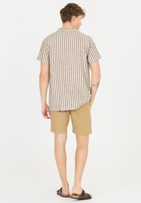 Kortärmad randig skjorta med krage, prydd med beige och marinblå vertikala ränder. I kombination med khakifärgade shorts och bruna slip-on sandaler.