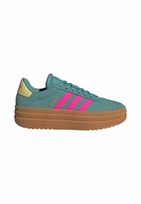Sneaker verde in suede con tre strisce rosa, dettagli crema e una suola in gomma spessa. Presenta un collare imbottito e una chiusura con lacci.