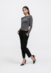Γκρι μπλούζα μακρυμάνικη με εφαρμοστή σχεδίαση, σε συνδυασμό με μαύρο παντελόνι καλοραμμένο. Το μοντέλο φοράει μαύρα γόβες με ψηλό τακούνι.