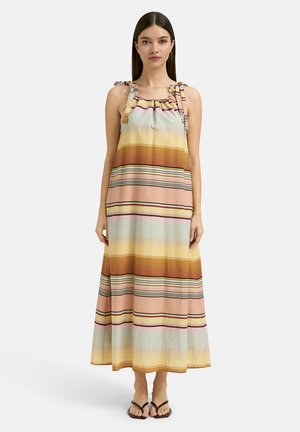 Woman wearing a sleeveless, ankle-length dress with horizontal pastel stripes and tie shoulder straps, paired with black sandals.