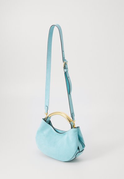 Turquoise suede handbag with a curved gold-tone metal handle, adjustable strap, and a smooth texture. Features a minimalist shape and design.