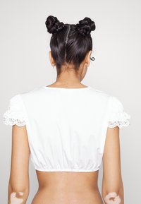 Hvid cropped top med elastisk kant, korte puffærmer og blondekant. Glat tekstur, tætsiddende design, afslørende ryg.