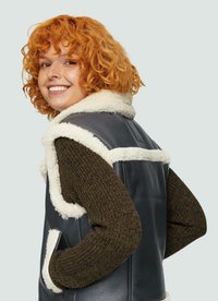 Dunkelbraune Lederweste mit einem cremefarbenen Lammfellkragen und -besatz, mit ärmellosem Design und Seitentaschen, vor einem hellen Hintergrund.