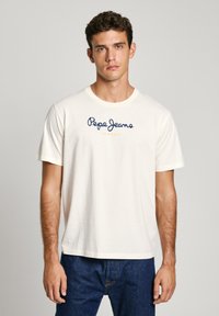 Kremajā krāsā kokvilnas t-krekls, kas rotāts ar zilu "Pepe Jeans" logo, zem kura dzeltenā krāsā ir uzraksts "LONDON". Īsas piedurknes un standarta apaļā kakla dizains.