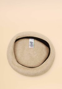 Világos bézs filc barett, lekerekített alakú. Fekete belső szalaggal és belül elhelyezett ápolási címkével. Puha textúra.