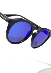 Crne sunčane naočale s velikim, uglatim okvirom i plavim zrcalnim lećama. Na dršci je metalni logo. Glatka površinska tekstura.