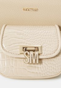 Beige handbag with a crocodile texture and a gold hardware clasp featuring "SM." The logo is positioned above on a smooth surface.