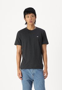 Mørk grå bomulls t-skjorte med korte ermer, rund hals og en liten logo på venstre side av brystet, kombinert med lyseblå jeans.