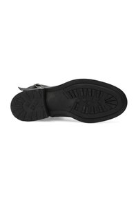 Suela de zapato de goma negra con surcos profundos para agarre, punta redondeada y detalle de correa con hebilla en el lateral.