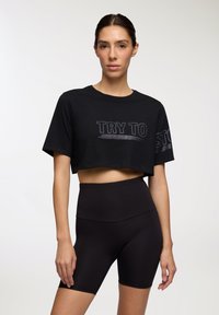 T-shirt cropped nero con grafica "TRY TO", abbinato a pantaloni ciclistici neri a vita alta. Entrambi realizzati in tessuto morbido e elasticizzato.