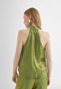 Top halter de satén verde con detalle de botón en la parte trasera y un suave brillo, combinado con pantalones texturizados a juego en verde. Acabado de superficie suave.