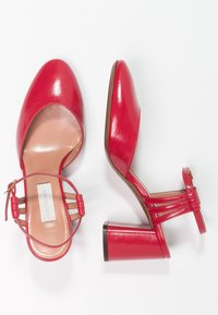 Chaussures à talons rouges avec une finition en cuir brillant, design à bout ouvert, bride à la cheville et talon bloc. Caractéristiques de détails de bande horizontale.