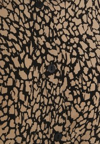 Tessuto beige con motivo astratto nero, caratterizzato da cinque bottoni neri. La texture appare liscia con una leggera lucentezza.