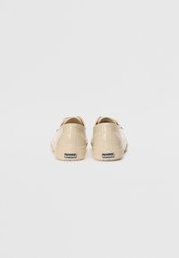 Beige lakkleathersneakers med en glatt tekstur, lavt design og gummisåler. Har en logo på hælen.