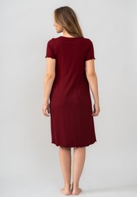 Burgundská šatová sukně ke kolenům, měkká tkanina, krátké rukávy s vlnitými okraji, těsně přiléhající střih, hladká textura, žádné viditelné vzory nebo akcenty.