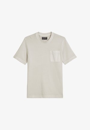 Jasno beżowa koszulka z krótkim rękawem wykonana z miękkiego materiału. Posiada kieszonkę na piersi, okrągły dekolt oraz minimalistyczny design bez wzorów.