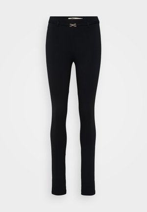 Schwarze, taillierte Leggings mit einer glatten Textur. Eng anliegende Form, mit einem goldenen Akzent am Bund. Keine sichtbaren Taschen.