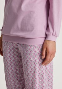Lichtroze sweatshirt met geribbelde boorden, gecombineerd met roze gestreepte pyjamabroek met bloemen- en bladdesigns. Zachte stofstructuur.
