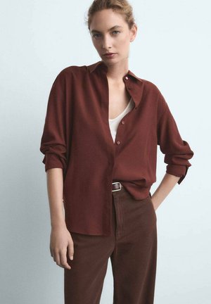 Camicia button-up bordeaux con maniche lunghe, vestibilità morbida e polsini risvoltati, abbinata a pantaloni marroni a vita alta con una texture liscia.