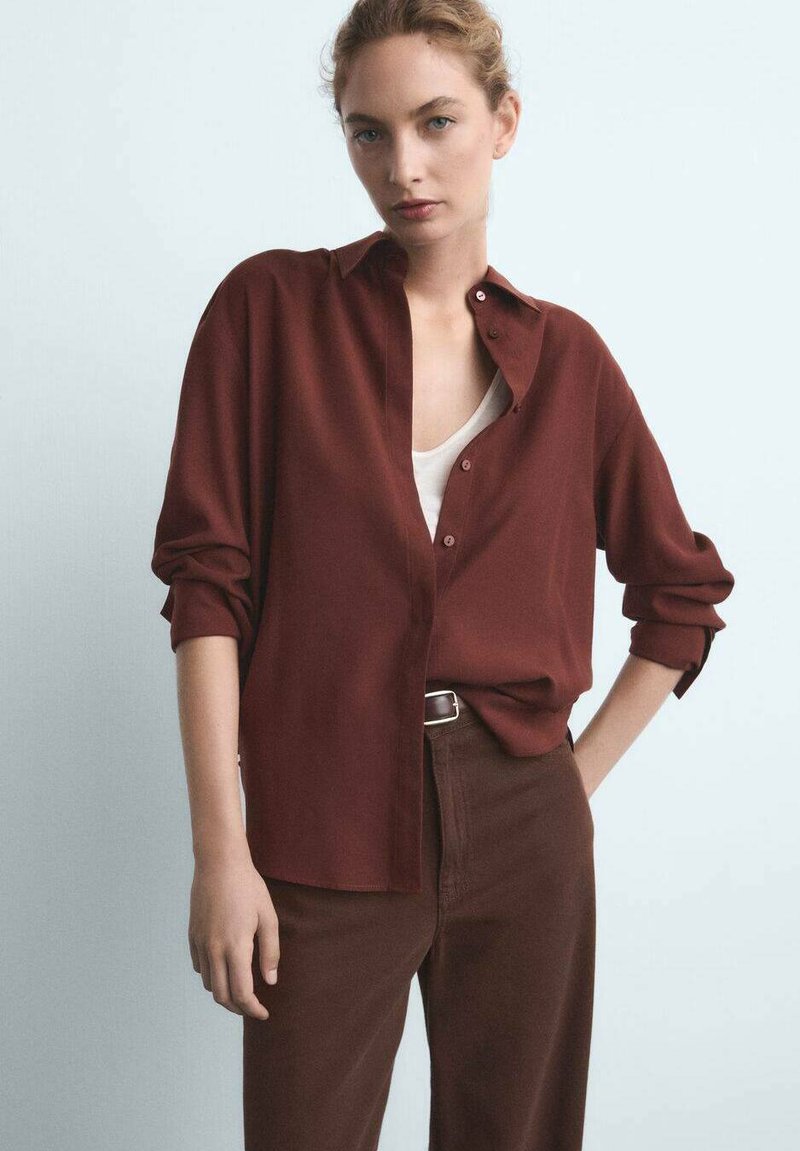 Chemise boutonnée bordeaux à manches longues, coupe décontractée, avec des poignets retroussés, associée à un pantalon taille haute marron, au toucher lisse.