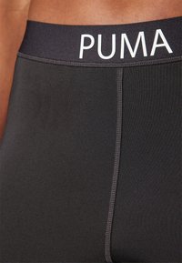 Shorts sportivi neri aderenti con una texture liscia. La vita elastica presenta il logo "PUMA" in bianco. Dettagli delle cuciture lungo il lato.