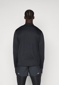Svart långärmad sporttröja med en slät yta, i kombination med mörka shorts. Har en enkel design utan framträdande mönster eller accenter.