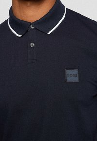 Polo shirt navy con design classico, presenta un colletto con rifinitura bianca, due bottoni e un tessuto testurizzato. Include un'etichetta con logo ricamato.