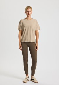 Beige short-sleeve top paired with brown leggings, featuring a smooth texture and fitted design, complemented by cream sneakers with black accents.