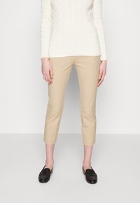Beige cropped byxor med en slät textur, kombinerade med en krämfärgad kabelstickad tröja. Skorna är svarta loafers.