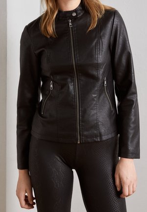Femme portant une veste en cuir noire ajustée avec fermeture éclair à l'avant et poches zippées, associée à un legging noir texturé.
