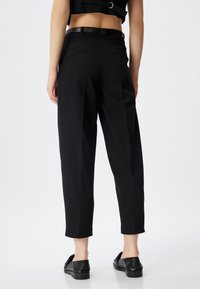 Pantaloni neri su misura con una vestibilità rilassata, caratterizzati da un tessuto liscio, fascia in vita, tasche laterali e una lunghezza cropped, abbinati a scarpe nere.