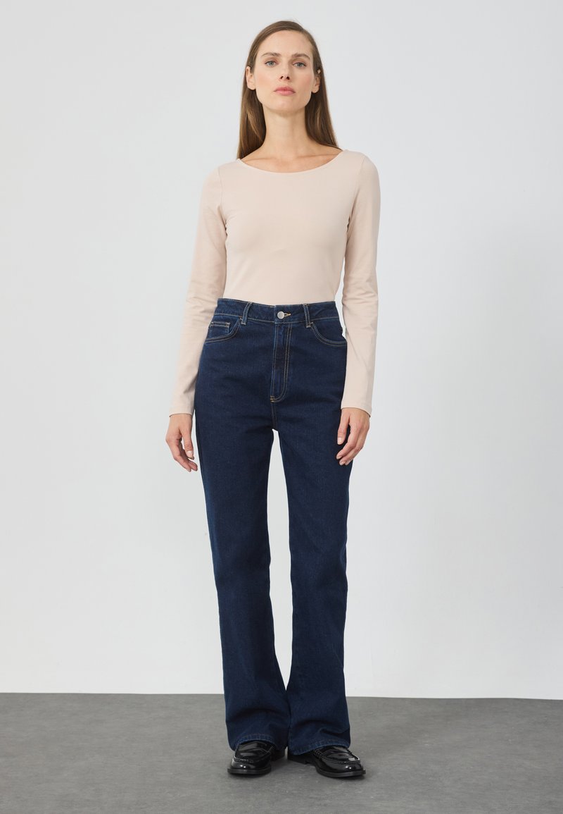 High-waisted dark blue jeans with flared legs, featuring front pockets, a button closure, and subtle stitching details. Smooth denim texture.