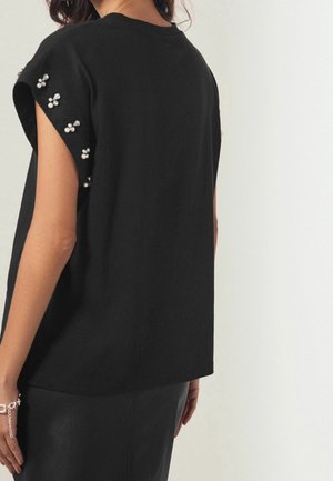 Czarna bluzka z krótkim rękawem zdobiona perłami i kryształkami na ramionach. Miękki, gładki materiał, luźny krój.