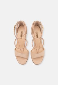 Sandalias de ante beige con un tacón grueso, que cuentan con tiras superpuestas, hebilla ajustable en el tobillo y detalles texturizados en las tiras.