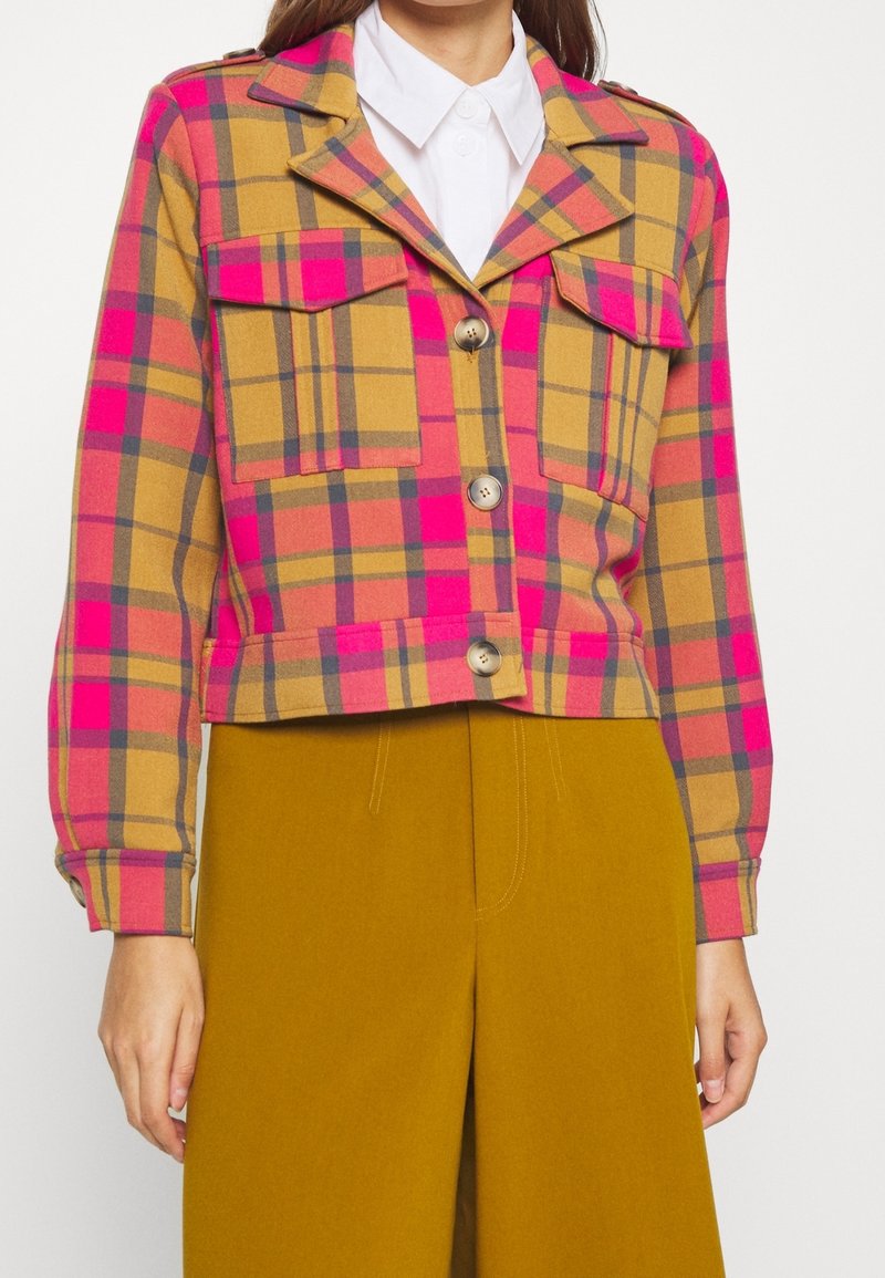 Veste à carreaux aux couleurs rose, jaune et gris, dotée de deux poches poitrine, de boutons et d'un col ouvert. Coupe courte, texture douce.