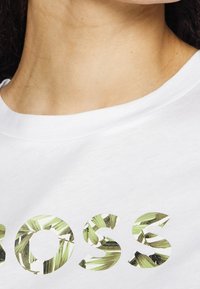 T-shirt bianca in cotone con la parola "BOSS" in lettere decorate con un motivo a foglia verde. Collo giroclassico e texture morbida.