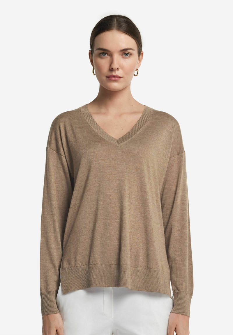 Beige v-ringad tröja i mjukt stickat material med långa ärmar, med en avslappnad passform och ribbade manschetter och fåll.