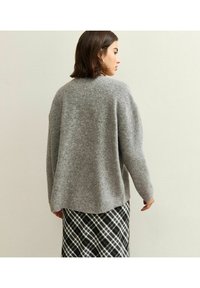 Suéter gris de punto con un corte relajado y dobladillo redondeado, con mangas largas. Combinado con una falda a cuadros en blanco y negro.