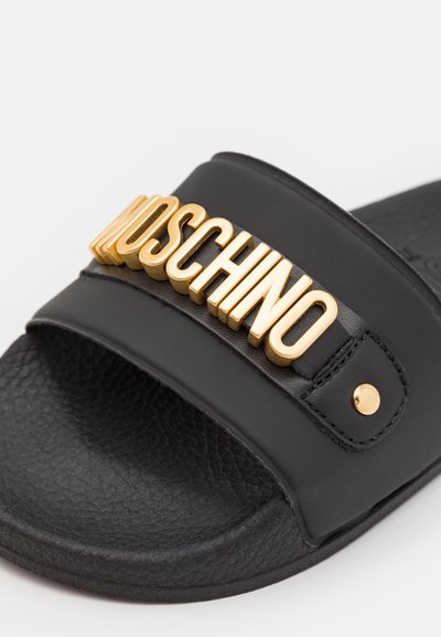 Schwarze Rutschsandale mit strukturierter Oberfläche, ausgestattet mit einem auffälligen goldenen "Moschino"-Logo auf dem Riemen und goldenen Hardware-Details.