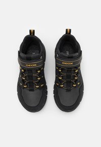 Czarne, lekkie sneakersy o gładkiej fakturze, z żółtymi akcentami, elastycznymi sznurówkami i rzepem. Posiadają wzmocniony czubek dla zwiększenia trwałości.