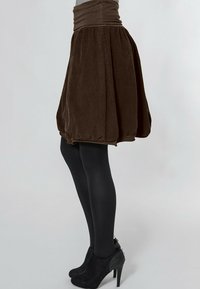 Brauer Samtrock mit gerafftem Design, tailliertem Bund und schwingendem Schnitt. Kombiniert mit schwarzen Strumpfhosen und hochhackigen Stiefeletten.