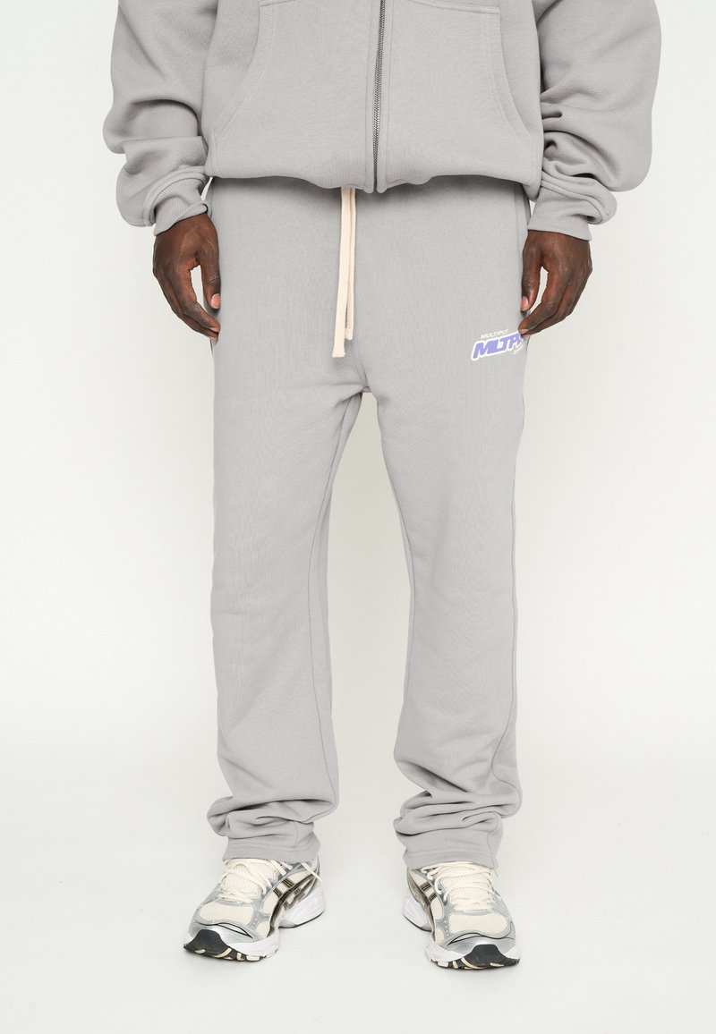 Pantalones de chándal grises de tejido suave con un ajuste relajado, cinturilla elástica con cordón y un pequeño logo colorido en el lado.