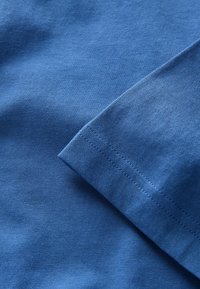 Sinine puuvillane kangas nähtava õmbluse detailiga äärel, mis näitab materjali tekstuuri ja kudumist.