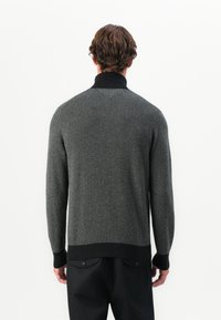 Suéter de punto en patrón espiga gris con cuello y puños negros. Cuenta con mangas largas y un corte relajado, tejido texturizado.
