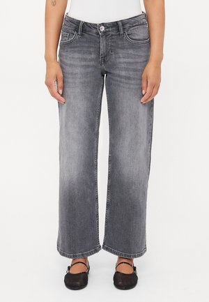 Jean en denim gris à jambes larges avec une texture légèrement délavée, présentant des poches avant et une fermeture à bouton. Style avec des ballerines noires.