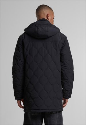 Schwarze gesteppte Jacke mit Kapuze, die eine glatte Außenfläche und runde Nahtmuster aufweist. Das Design ist oversized mit langen Ärmeln.