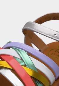 Sandale en cuir multicolore avec des lanières superposées en blanc, rouge, jaune, vert et violet, dotée d'une semelle marron et d'une bride à la cheville.