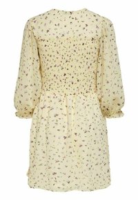 Kukkakuosisessa keltaisessa mekossa on smokkibodice, pitkät puffihihat ja pehmeä, kevyt rakenne. Takakuvassa näkyy rypytetty yksityiskohta.